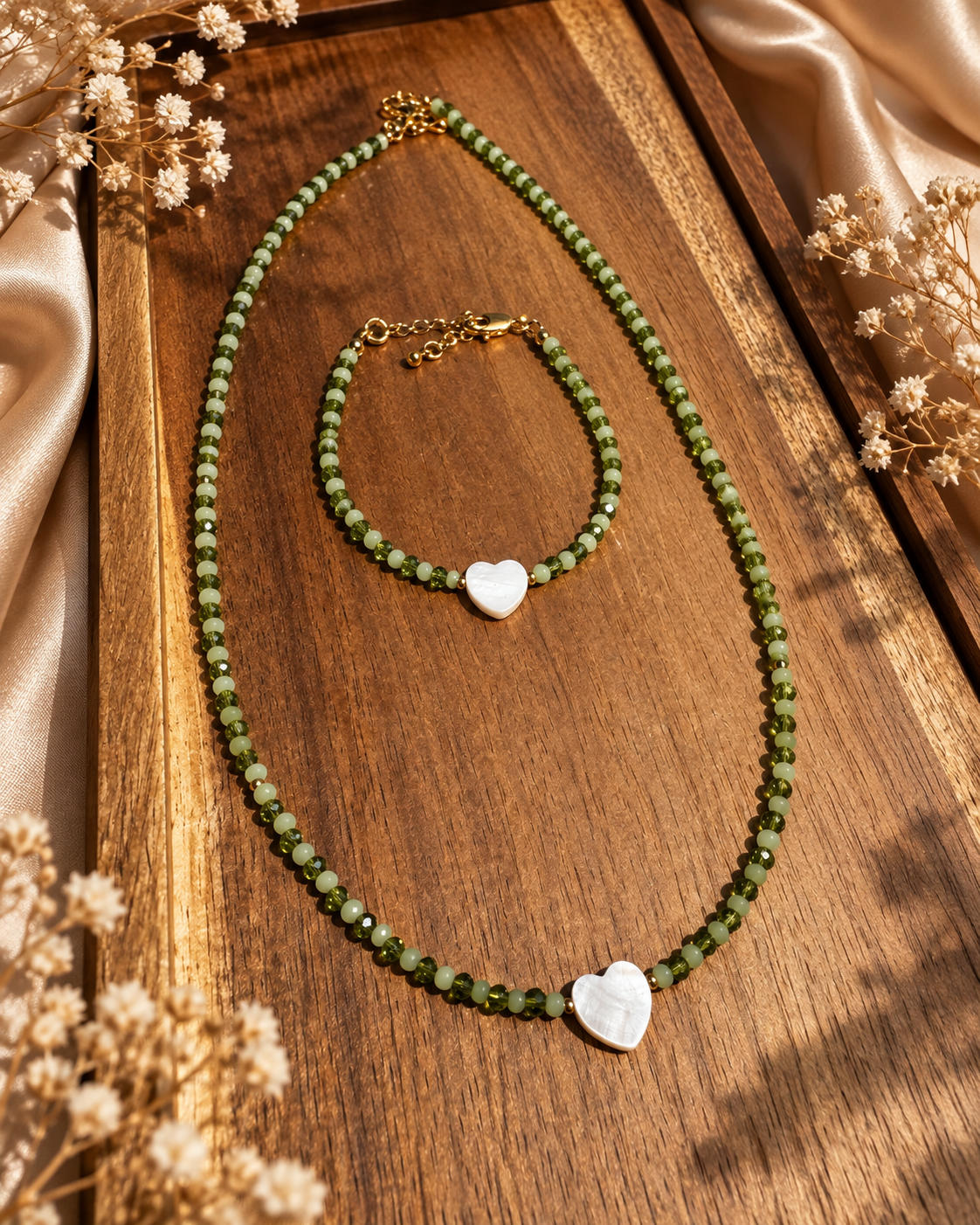 Green glass necklace & bracelet on a wooden tray surrounded by champagne fabric