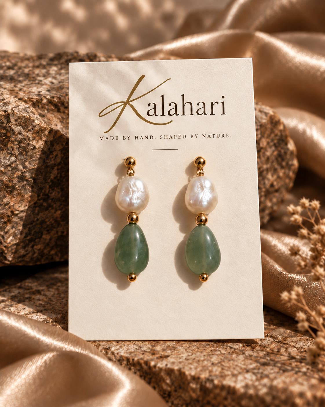 Pearl and green stone drop earrings on an ivory Kalahari card surrounded by textured stone and champagne fabric