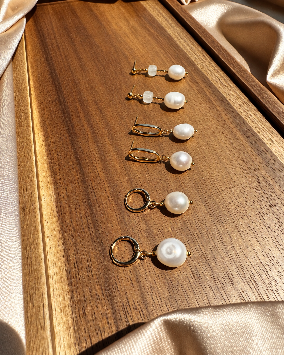 Three pairs of pearl drop earrings with gold-plated hardware arranged on a wooden tray