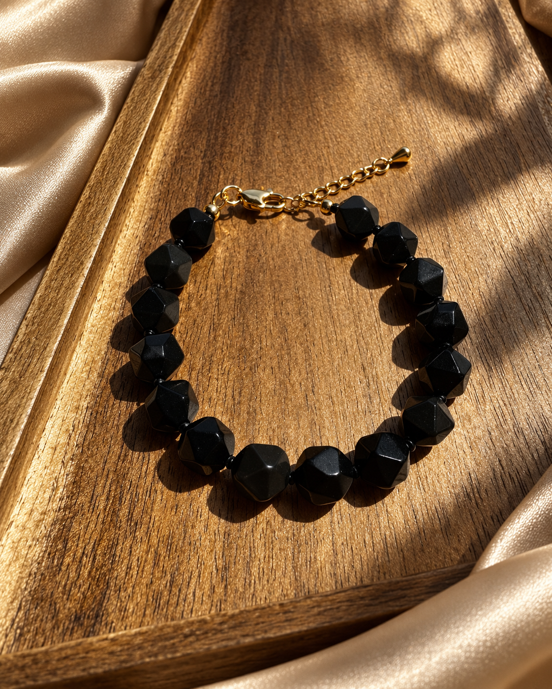 Black stone bracelet displayed on a wooden tray with champagne fabric