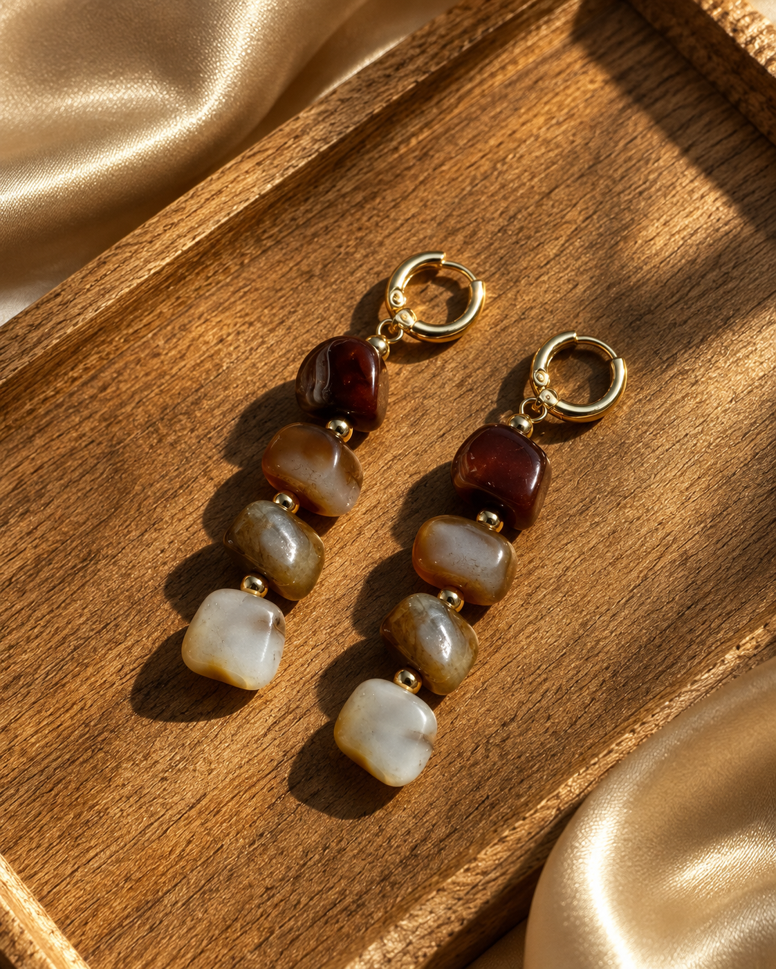 Earth-tone drop earrings displayed on a wooden tray with champagne fabric
