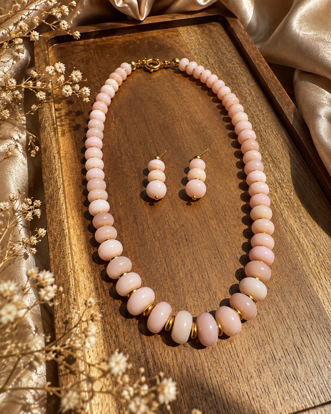 Blush stone necklace and matching earrings with gold-plated details on a wooden tray