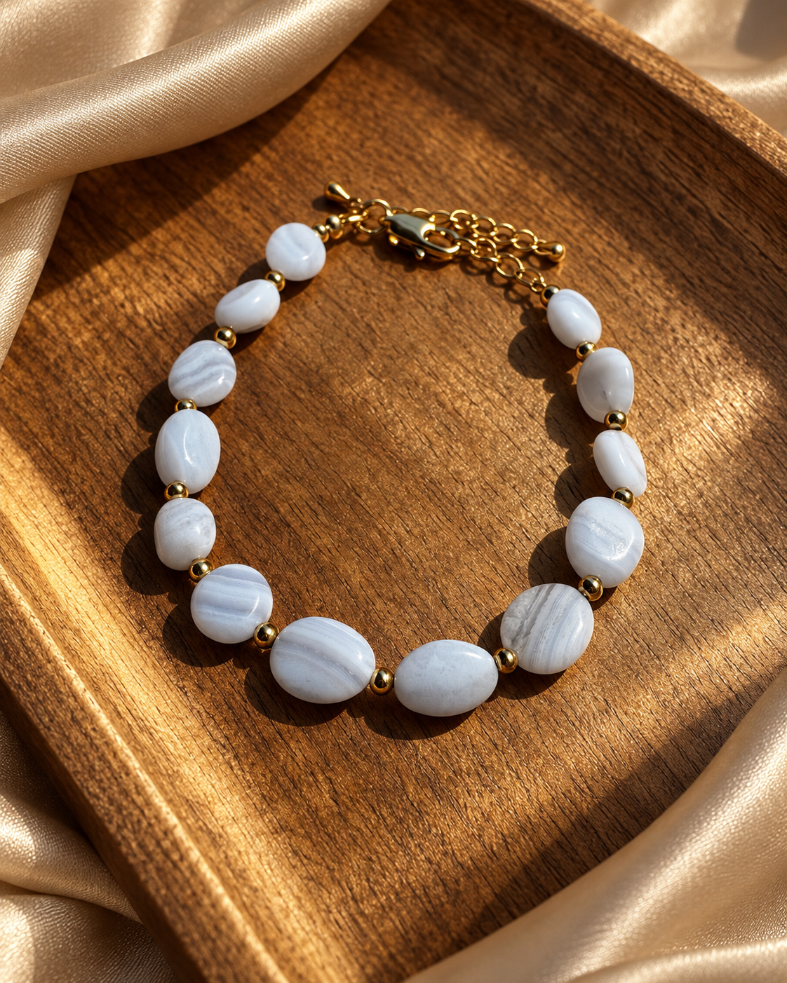 Pale blue stone bracelet displayed on a wooden tray with champagne fabric